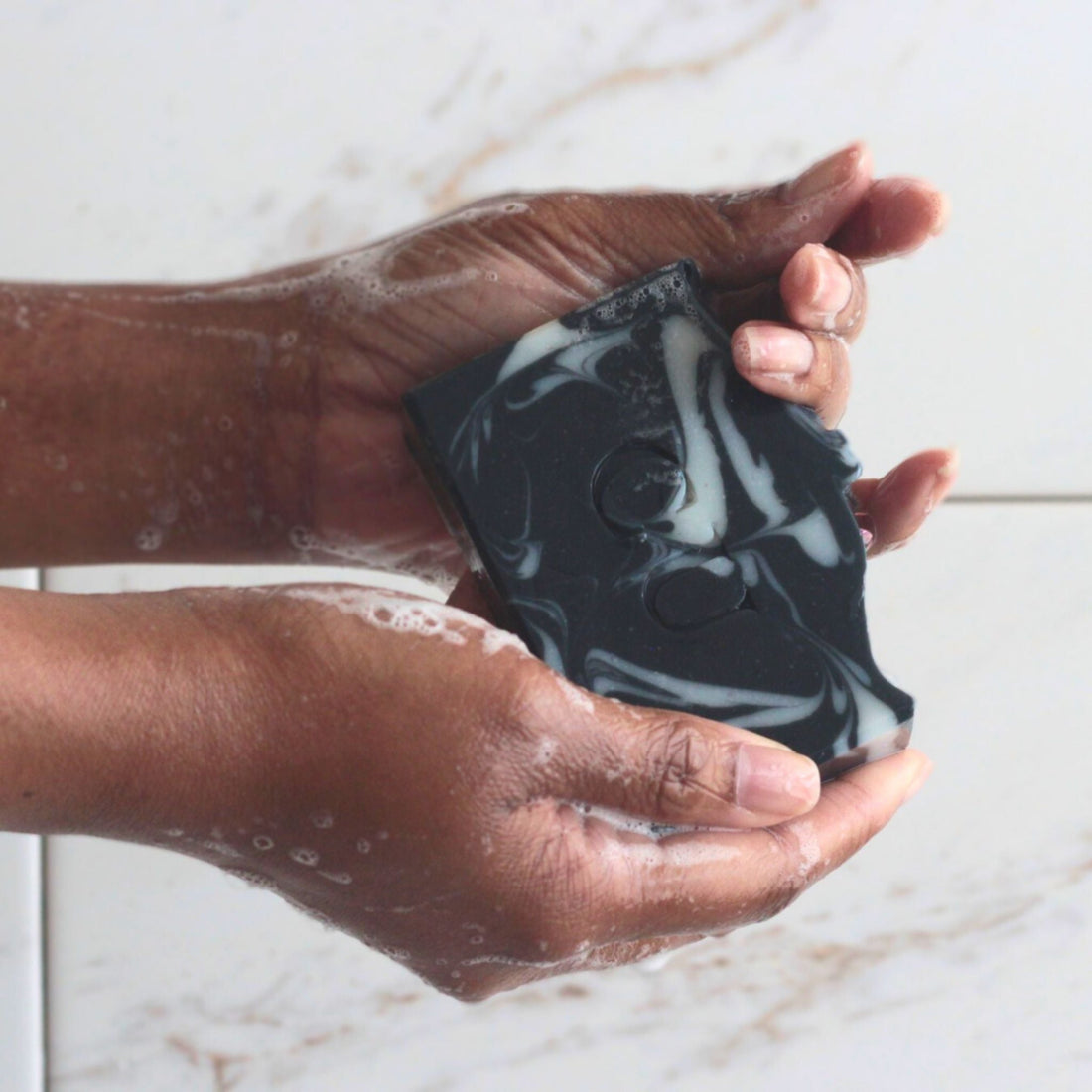 Hands holding a wet bar of all natural charcoal + peppermint soap. Cherish U®