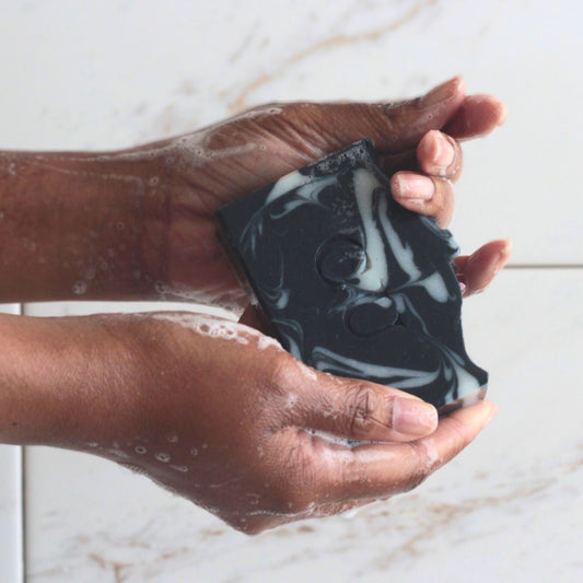 Hands holding a wet bar of all natural charcoal + peppermint soap.