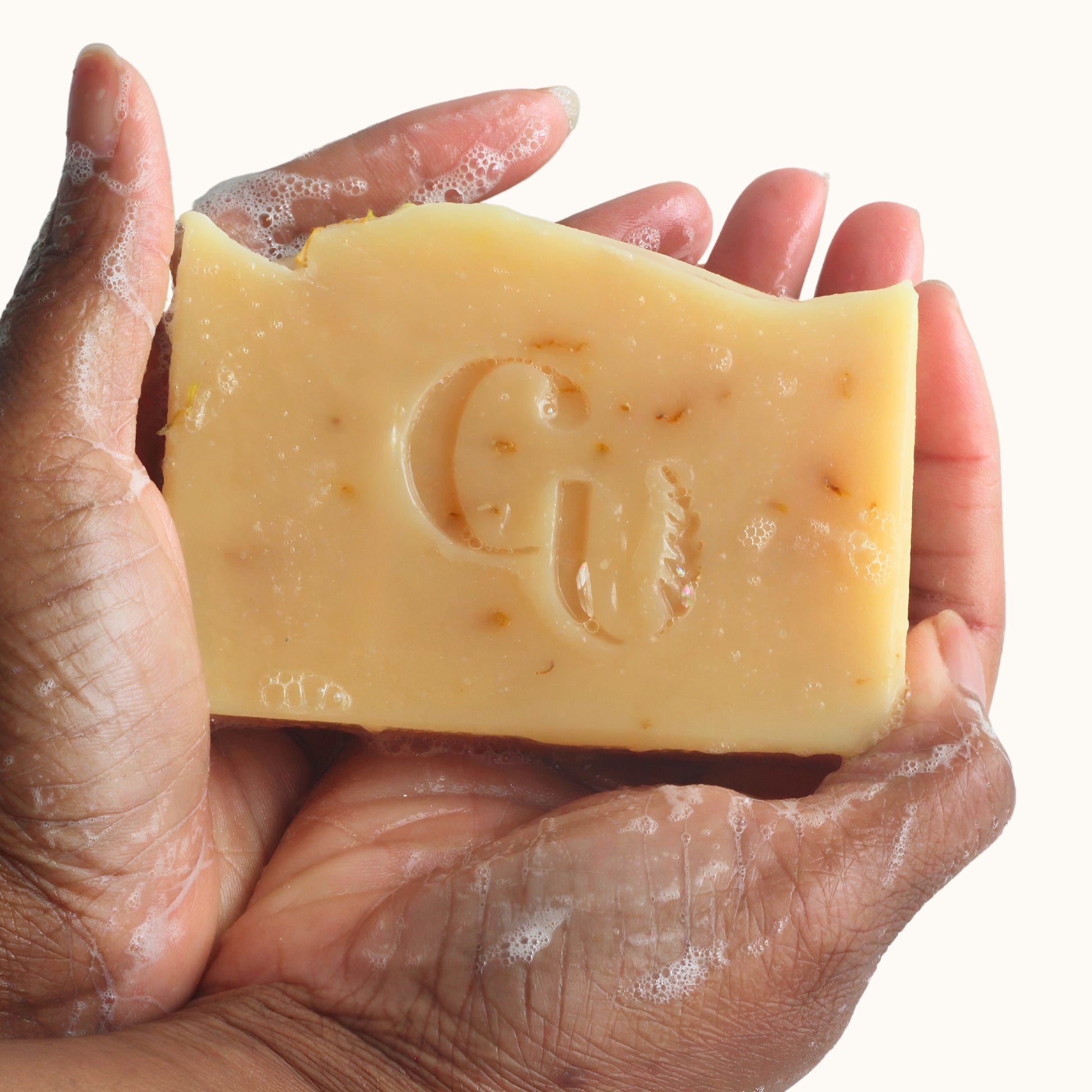A soapy hand holding a bar of Citrus + Mint soap, foaming up with a fresh, invigorating citrus-scented lather