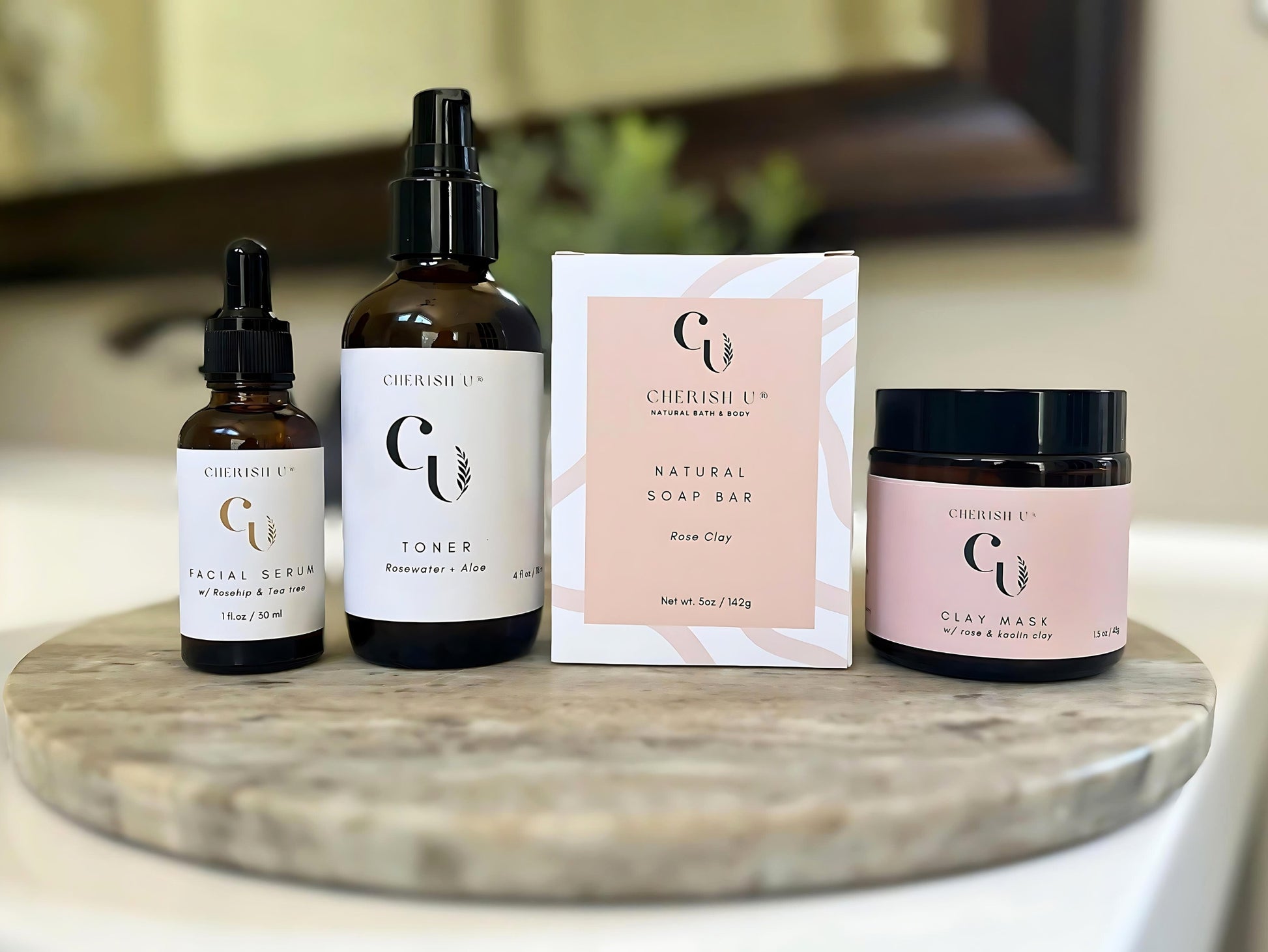 A revitalizing skincare set featuring a rose clay soap, rose clay + kaolin clay mask, rosewater + aloe toner, and facial serum with rosehip and tea tree oil on a bathroom vanity.