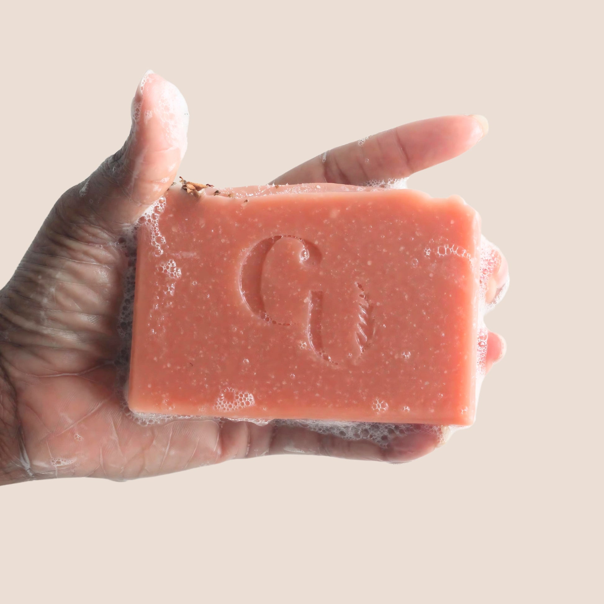 A soapy hand holding a bar of Rose Clay soap, lathering up with a soft, white foam, offering a gentle cleansing experience.