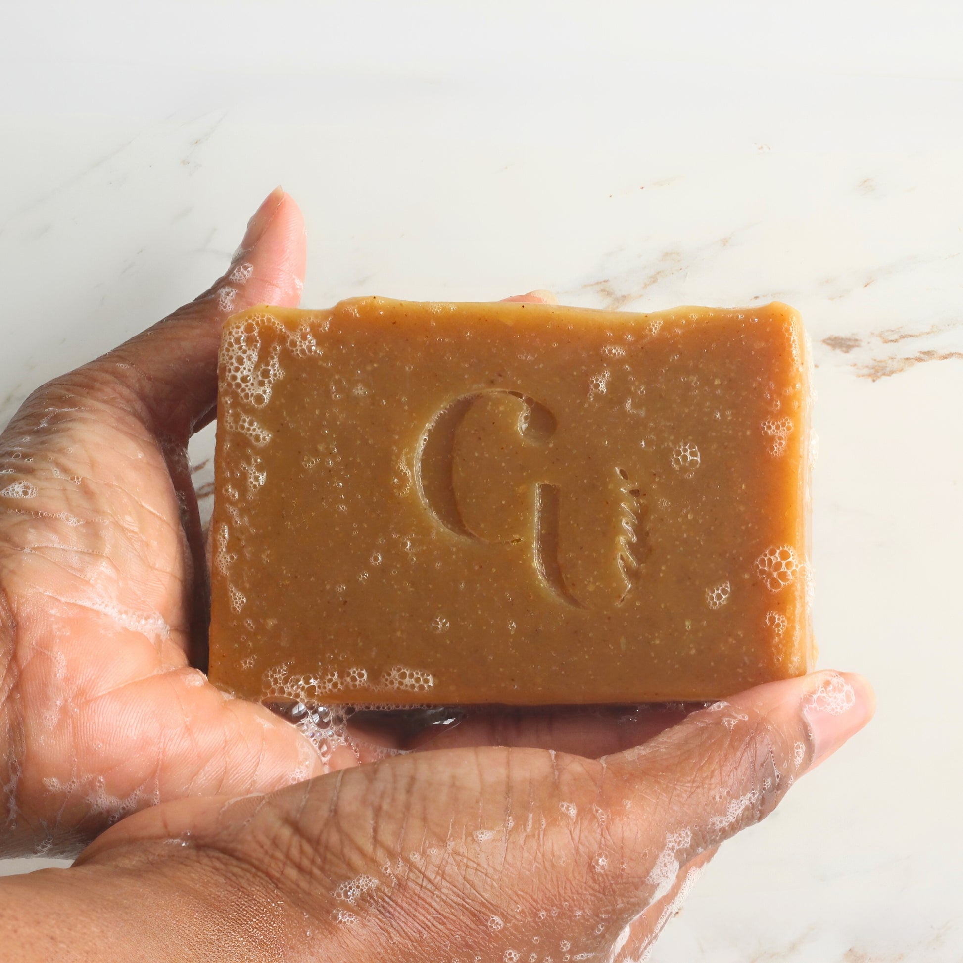 A soapy hand holding a bar of Turmeric soap, covered in a lather.