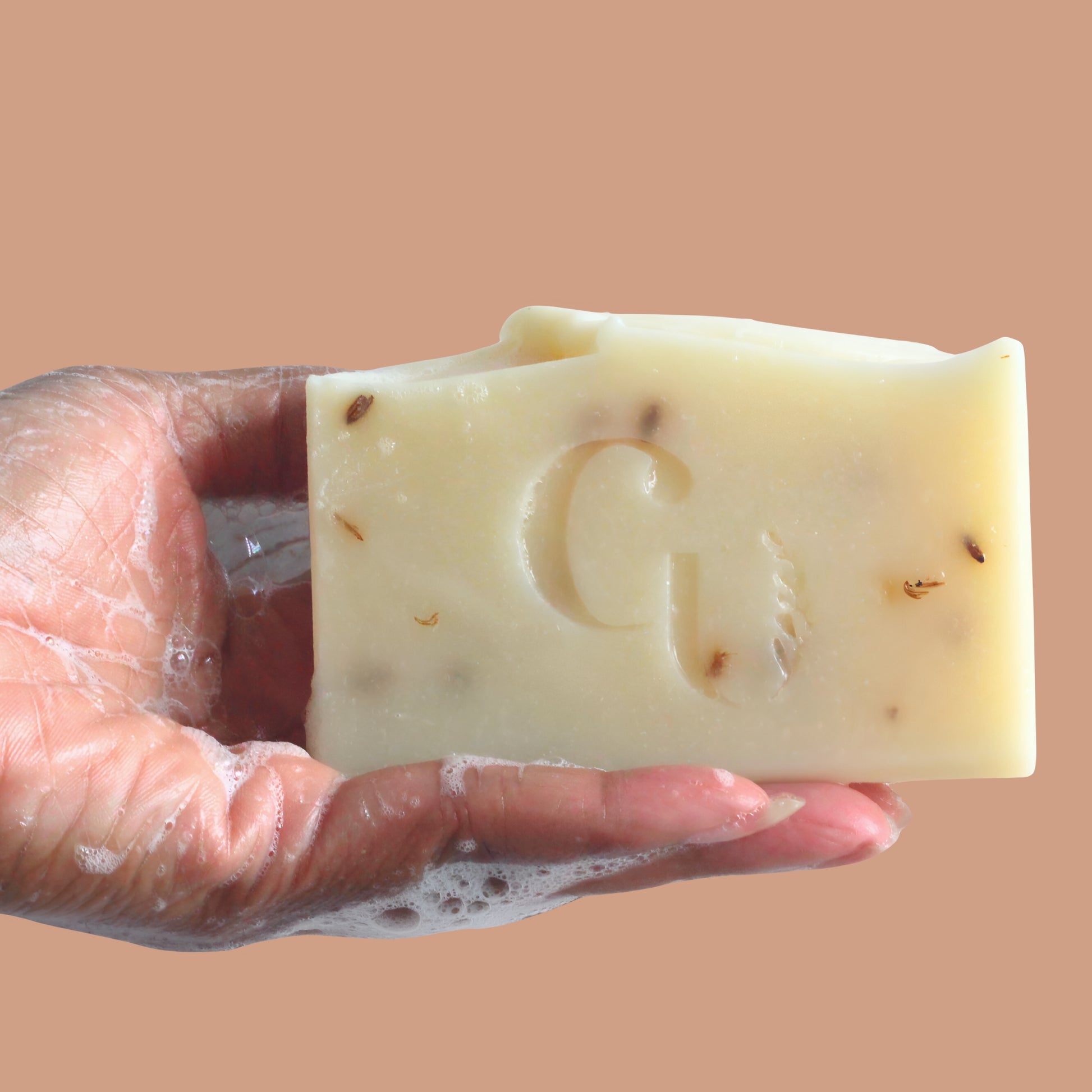 A soapy hand holding a bar of Coconut Shea soap, covered in creamy lather, hinting at deep hydration