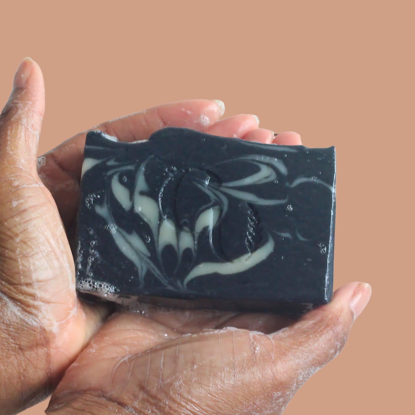 A soapy hand holding a bar of Charcoal + Peppermint soap, creating lather with a hint of minty freshness. Cherish U®