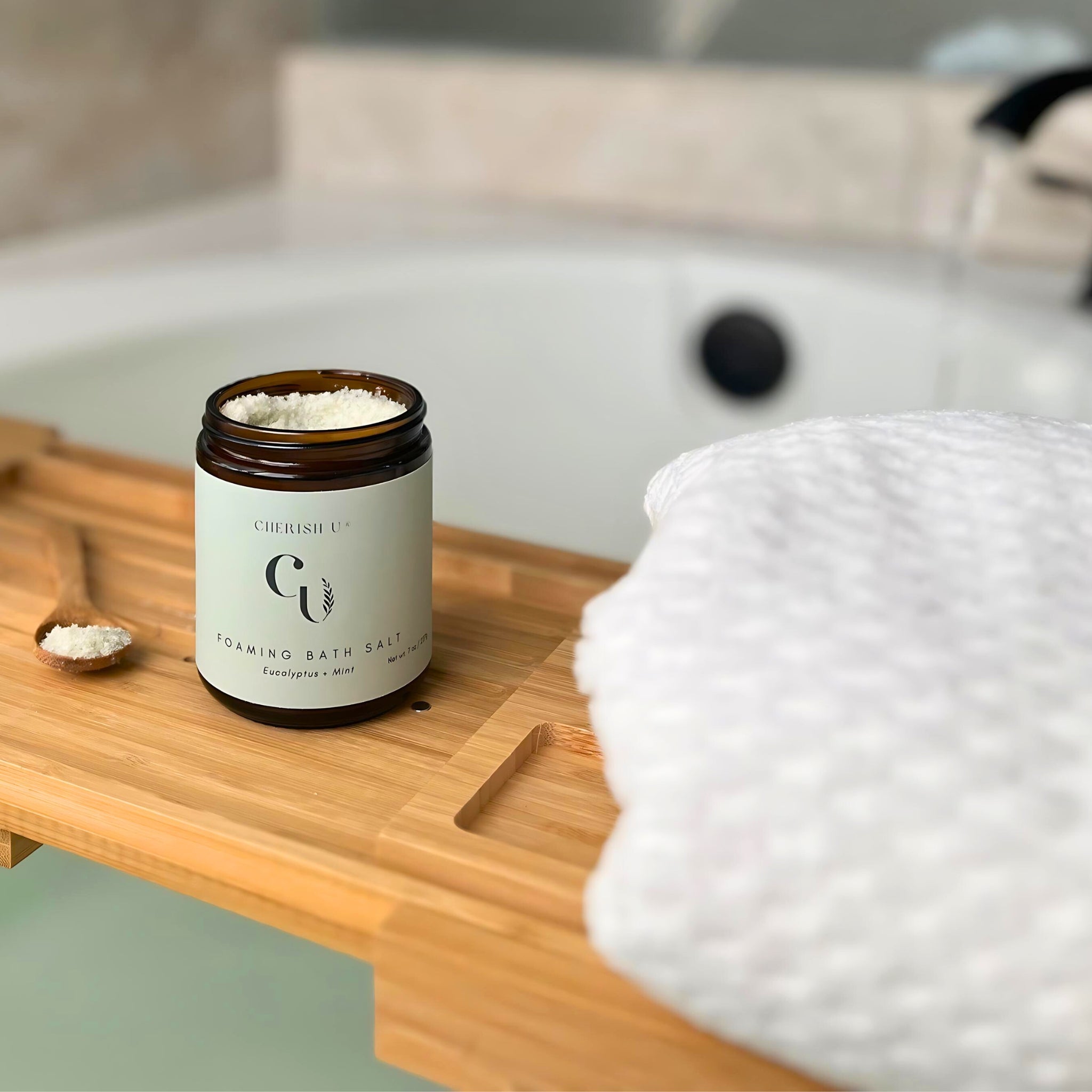 A jar of Eucalyptus foaming bath salts is placed stylishly on a wooden bathtub tray. The sound of running water in the background adds to the refreshing and invigorating scene