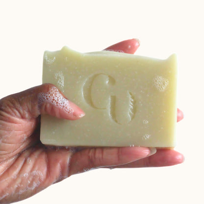 A soapy hand holding a bar of French Green Clay soap, covered in a gentle, cleansing lather with tea tree and lavender