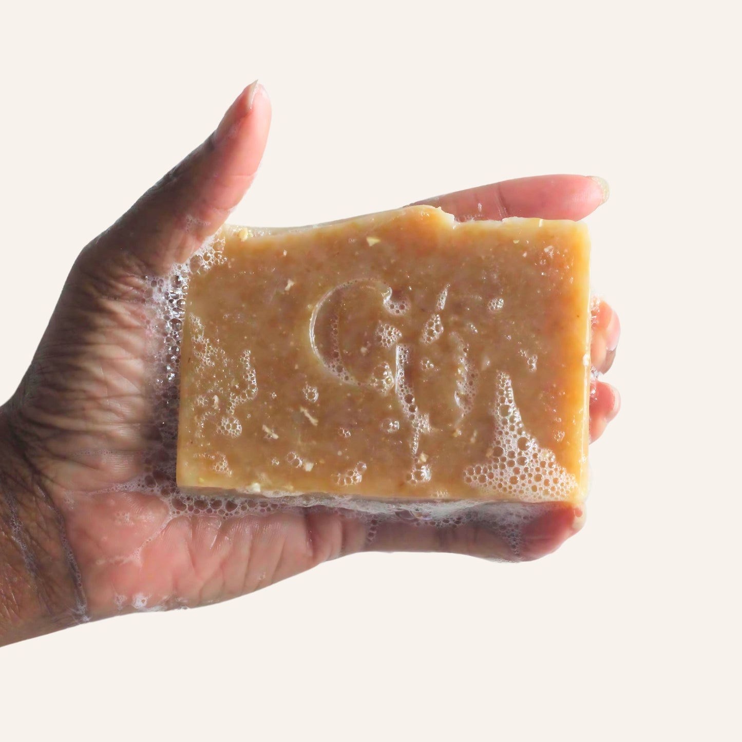 A soapy hand holding a bar of Goat Milk + Honey Oat soap, producing a rich, nourishing lather with oat flecks visible Cherish U®