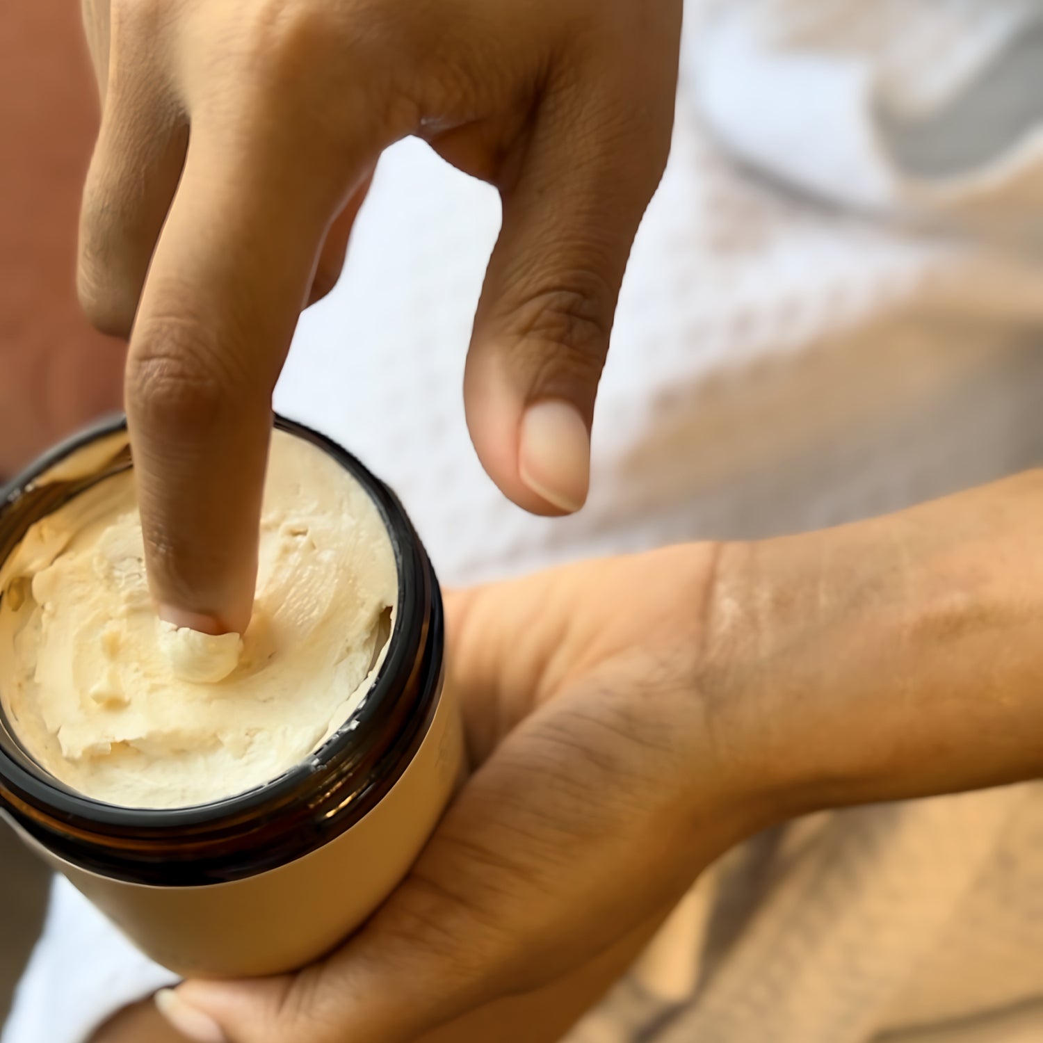 A persons finger dipped in body butter made with Shea, cocoa, and mango butters showing off its whipped texture.