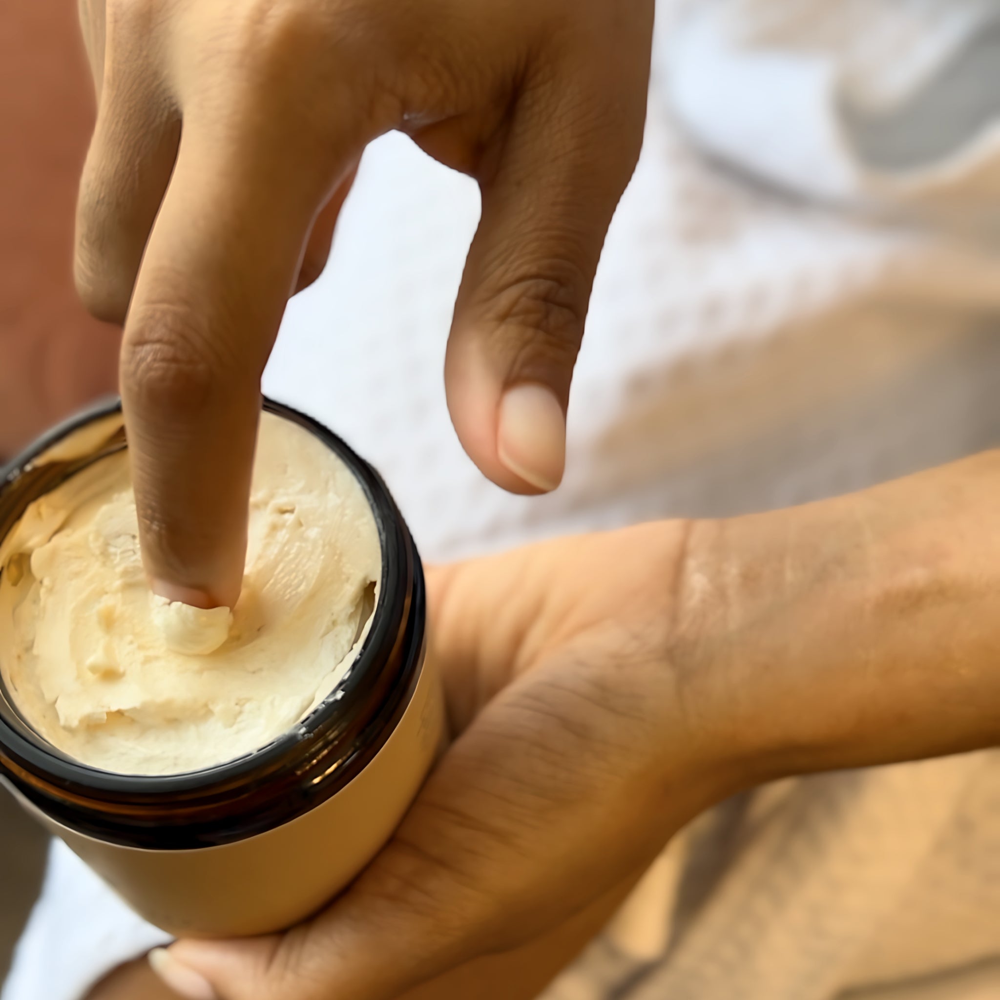 A persons finger dipped in body butter made with Shea, cocoa, and mango butters showing off its whipped texture.